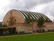 A building with a curved roof, young trees and a lawn in front